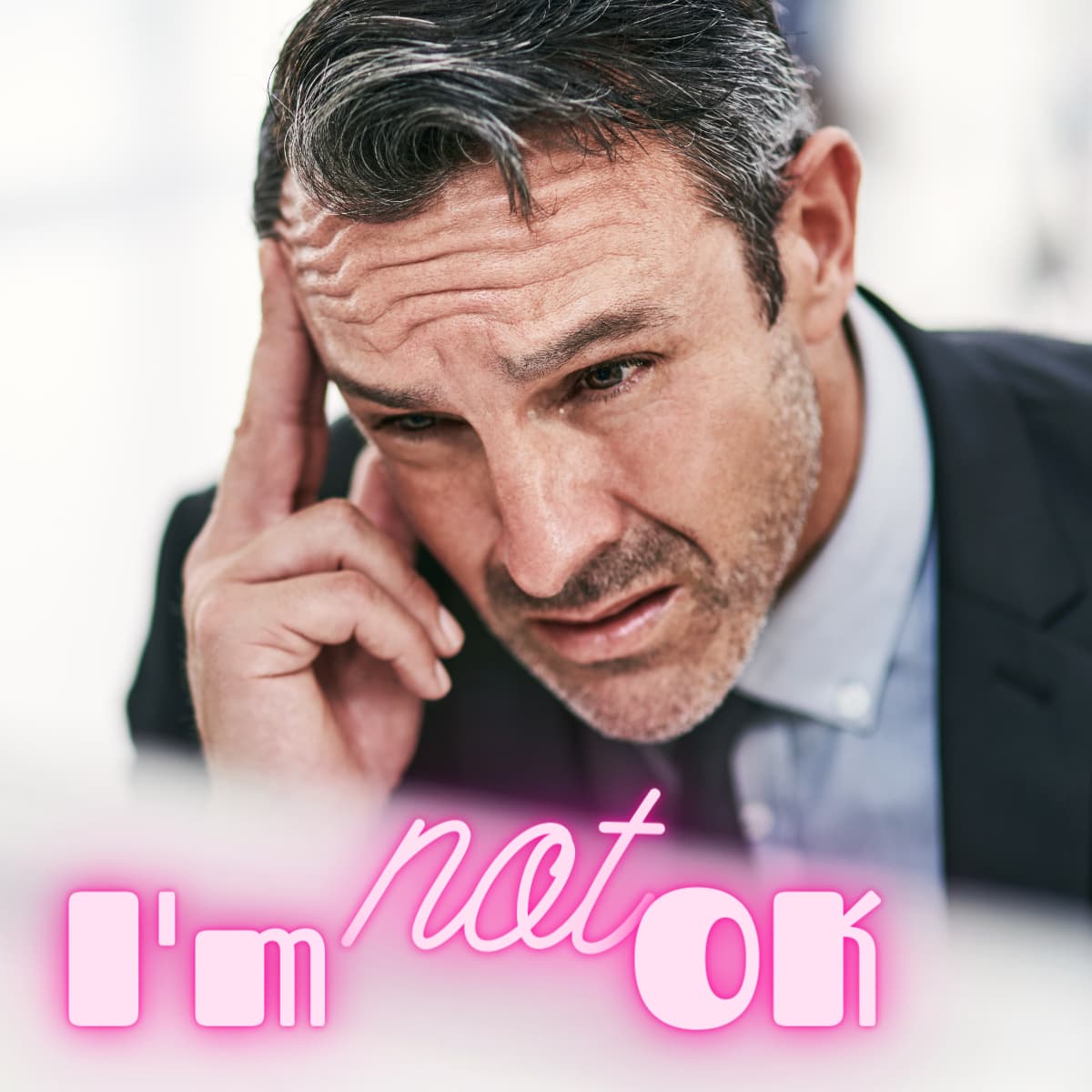 I’m not OK A worried man in a suit touches his temple, looking stressed. The neon text overlay reads Im not OK in pink and white letters.