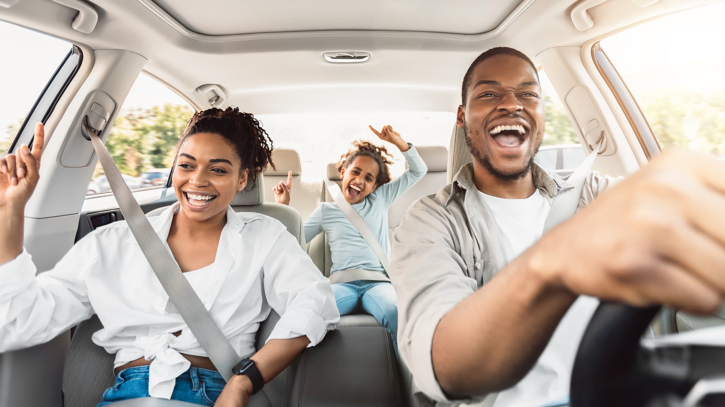 A cheerful family of three, with a man driving, a woman in the passenger seat, and a child in the back, all smiling and dancing while enjoying a sunny car ride after their ADHD Evaluations and Coaching session.