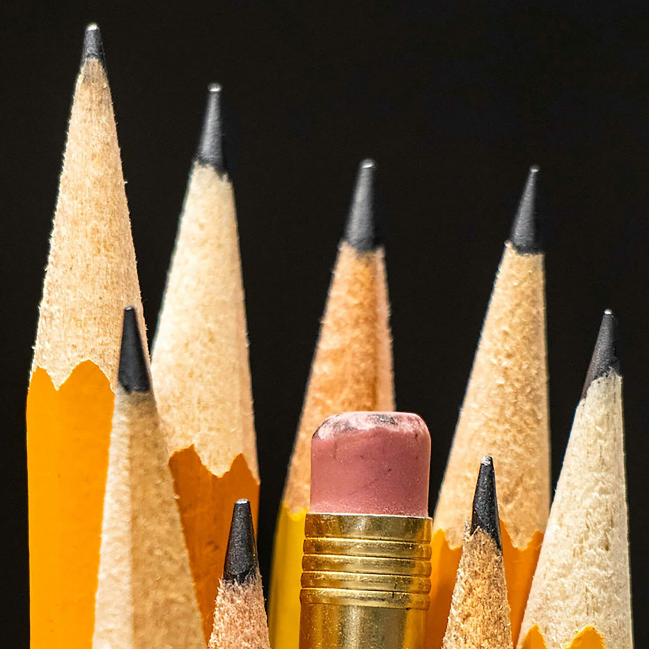 ADHD Eval Close-up of several sharpened yellow pencils with one pencil, showing a used pink eraser, positioned upside down among them. The background is dark, highlighting the pencils points and textures.